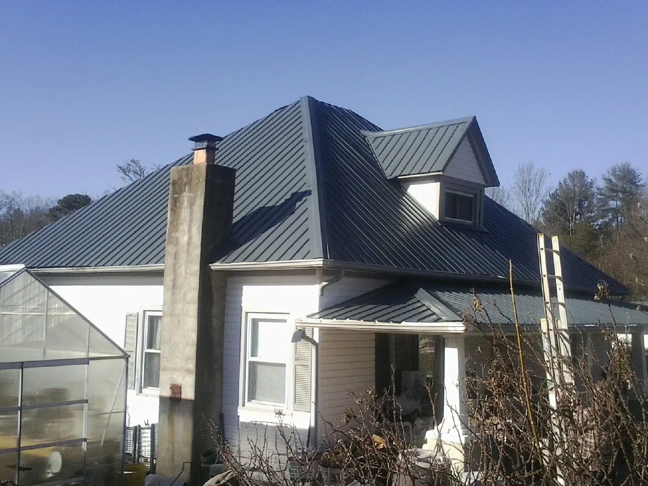 Dark blue standing seam metal roof on a white farmhouse with dormer — Slate & Tile Roof Repair by Roofing Brothers in Loyalhanna