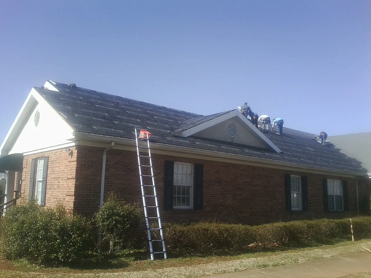 Crew tearing shingles off a brick ranch roof with a ladder set — Emergency Roof Repair work by our crew in Loyalhanna