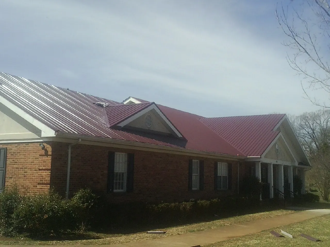 Red metal roof with gabled entries on a long brick building, from a Hail Damage Roof Repair job in Loyalhanna