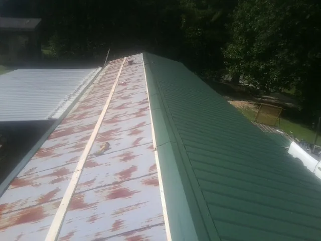 Old rusted panels beside newly installed green metal roofing — Wind Damage Roof Repair by Roofing Brothers in Loyalhanna