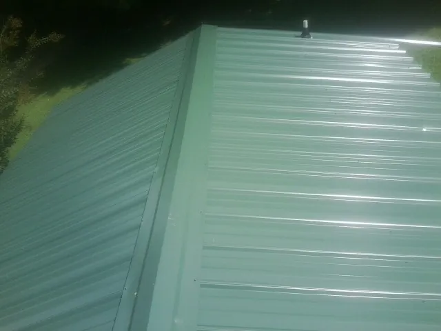 New green metal panels meeting at the ridge of a roof — Flat Roof Repair work by our crew in Loyalhanna