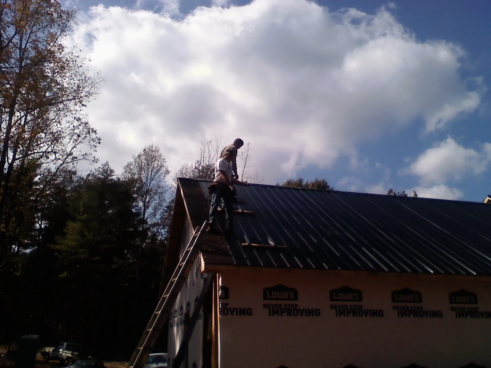 Roofer fastening dark metal panels high against a cloudy sky, from a Roof Inspection job in Loyalhanna