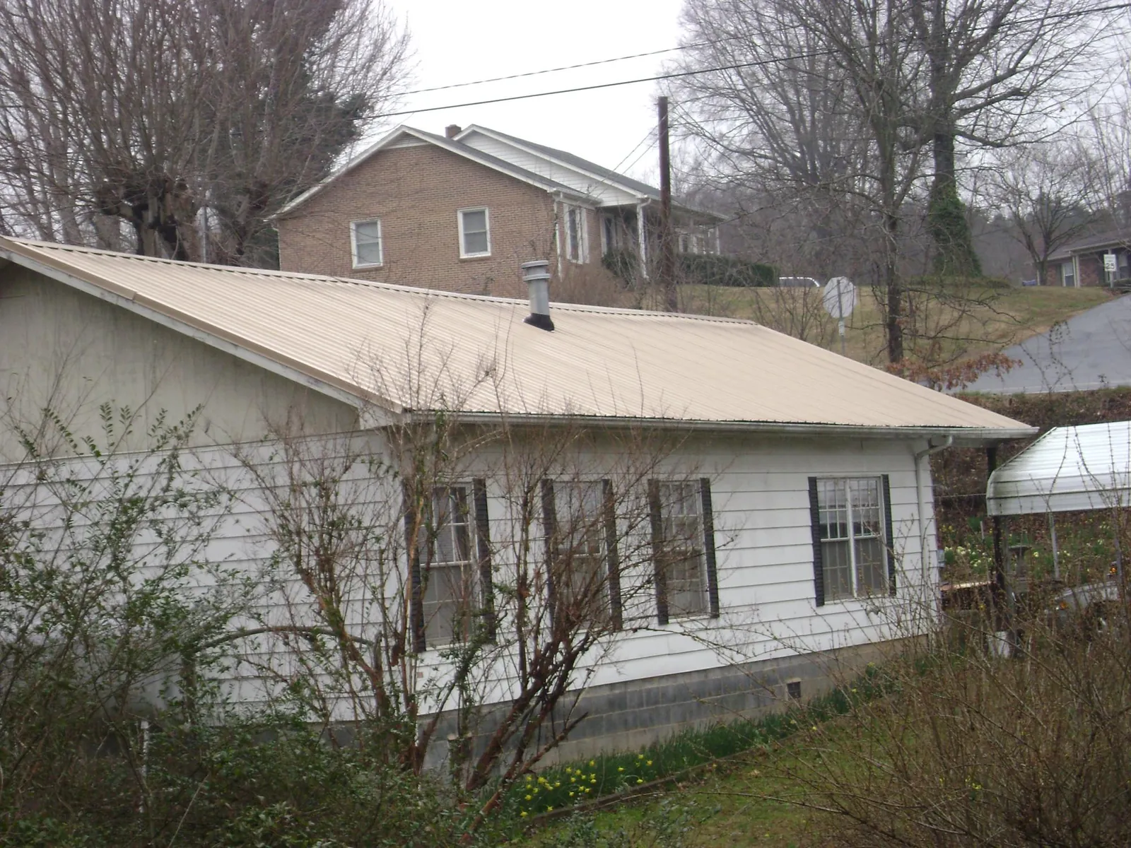 Tan metal roof on a white sided house set into a hillside — Commercial Roofing by Roofing Brothers in Loyalhanna
